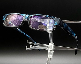 May include: Blue and black patterned reading glasses with a clear plastic frame. The glasses are on a clear plastic stand.