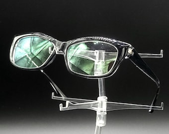 May include: Black plastic framed glasses with green tinted lenses. The glasses are on a clear plastic stand.