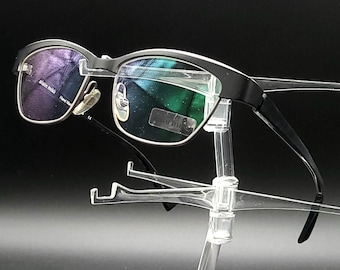May include: Black framed glasses with a dark blue and green lens on a clear plastic stand.