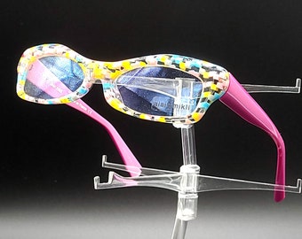 May include: A pair of pink and multi-colored patterned glasses with a pink frame on a clear plastic display stand.