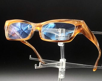 May include: Brown tortoise shell eyeglasses with blue tinted lenses. The glasses are on a clear plastic display stand.