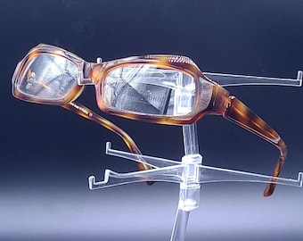 May include: Tortoise shell reading glasses with a clear lens on a clear plastic stand.