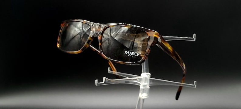 Puede incluir: Gafas de sol de carey con lentes marrones. Las gafas tienen un acento met&aacute;lico en el puente y el nombre de la marca "SHARCK" est&aacute; impreso en la lente derecha.