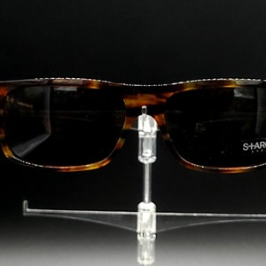 Puede incluir: Gafas de sol de carey con lentes negros. Las gafas tienen el logotipo "SHARCK" en la lente derecha.