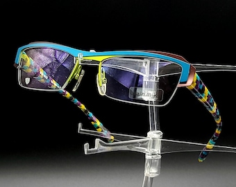 May include: A pair of colorful eyeglasses with a blue, yellow, and black patterned frame. The glasses are on a clear plastic stand.