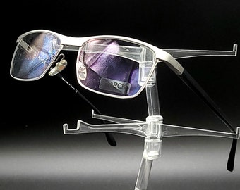 May include: Silver and black rectangular frame eyeglasses with blue tinted lenses. The glasses are displayed on a clear plastic stand.