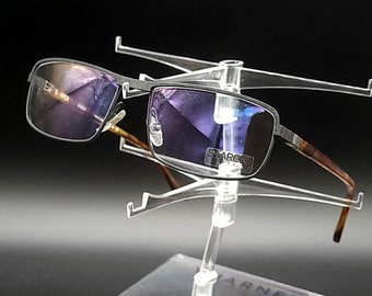 May include: A pair of silver-toned rectangular eyeglasses with dark purple lenses. The glasses are displayed on a clear plastic stand.