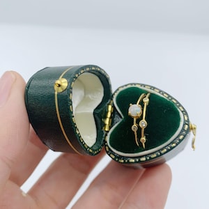 May include: A gold ring with a white opal gemstone and small clear gemstones set in a heart-shaped green velvet ring box.