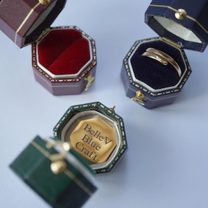 May include: Three ring boxes, one red, one blue and one green. The green box is open and shows a gold ring with the inscription "Belle V Blue Craft".