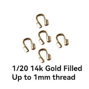 May include: Five gold-filled jewelry clasps. Each clasp is U-shaped with two rectangular ends. The text reads "1/20 14k Gold Filled Up to 1mm thread". These clasps are designed for jewelry making and crafting.