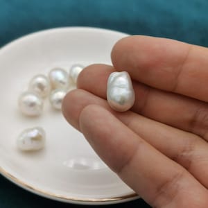 Op de afbeelding: Een groep witte barokparels, sommige liggen in een witte schaal en een wordt in de hand gehouden.
