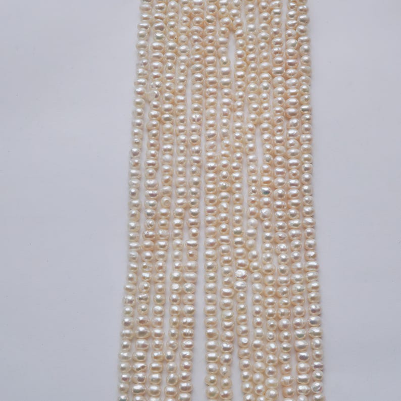 May include: A strand of white freshwater pearls, approximately 4-5mm in size. The pearls are strung on a thin thread and are ready to be used for jewelry making.