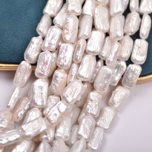 May include: A strand of white baroque freshwater pearls with an iridescent sheen. The pearls are rectangular in shape and have a natural, irregular texture.