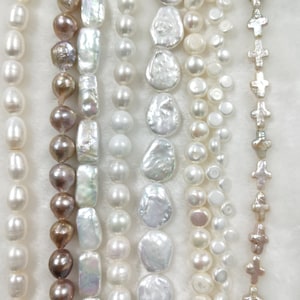Peut inclure: Un assortiment de perles blanches et brunes, y compris des formes rondes, ovales et irrégulières, sont enfilées sur un fond blanc. Il y a aussi une rangée de perles en forme de croix argentées.