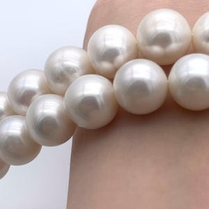 May include: A strand of white pearls, each pearl is round and smooth. The pearls are arranged in a line, with the largest pearl in the centre.