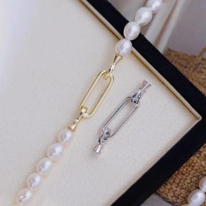 May include: A pearl necklace with a gold chain link and a silver chain link. The necklace features white oval pearls. The gold chain link is connected to the pearls. The silver chain link is separate.