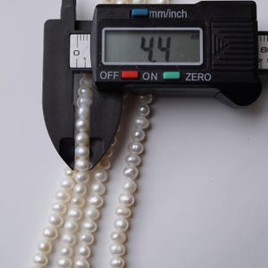 May include: A close-up of a white pearl necklace being measured with a digital caliper. The caliper reads 4.4 mm.
