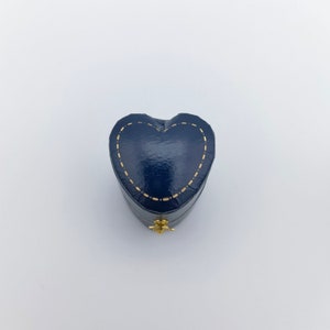 Pu&ograve; includere: Una piccola scatola a forma di cuore in velluto blu con cuciture dorate. La scatola ha un coperchio incernierato e una piccola chiusura dorata.