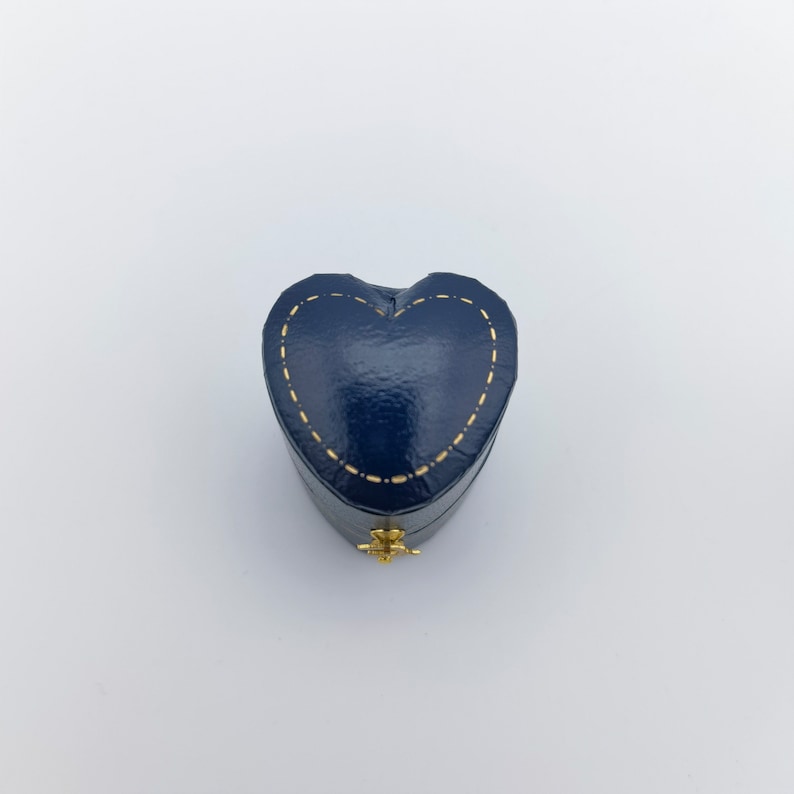 Pu&ograve; includere: Una piccola scatola a forma di cuore in velluto blu con cuciture dorate. La scatola ha un coperchio incernierato e una piccola chiusura dorata.