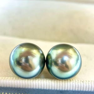 Peut inclure: Deux perles rondes, iris&eacute;es, de couleur sarcelle. Les perles ont une surface lisse et r&eacute;fl&eacute;chissante, avec des reflets dor&eacute;s et argent&eacute;s. Les perles sont pr&eacute;sent&eacute;es sur une surface bleu clair et blanche.