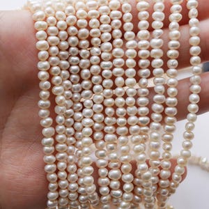 May include: A strand of white freshwater pearls, strung on a thin thread. The pearls are small and round, with a smooth, glossy finish.