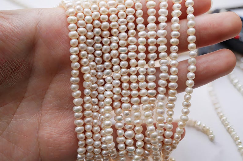 May include: A strand of white freshwater pearls, strung on a thin thread. The pearls are small and round, with a smooth, glossy finish.