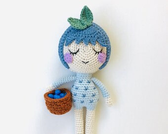 May include: A handmade crochet doll with blue hair, a green leaf, and closed eyes. The doll wears a light blue outfit and holds a brown basket filled with blue berries. The doll is approximately 6 inches tall.