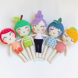 Pode incluir: Cinco bonecas de crochê com cabelo e roupas de diferentes cores. As bonecas estão todas sorrindo e com os olhos fechados. As bonecas estão dispostas em círculo sobre um fundo branco. As bonecas usam roupas diferentes, incluindo um vestido listrado verde e branco, um vestido listrado azul e branco, um vestido rosa e branco, um vestido roxo e branco e um vestido amarelo e branco. As bonecas medem todas aproximadamente 25 cm de altura.