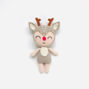 Puede incluir: Un juguete de reno de crochet con un cuerpo marrón, detalles blancos y una nariz roja. El reno tiene una cara sonriente con los ojos cerrados.