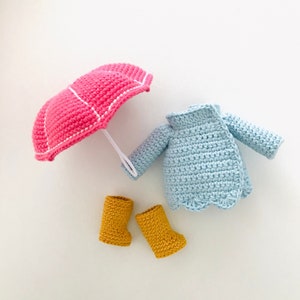 May include: A crocheted doll outfit set with a pink umbrella, blue jacket, and yellow boots.