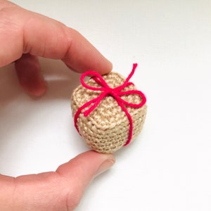 May include: A small crocheted gift box tied with a bright pink ribbon.