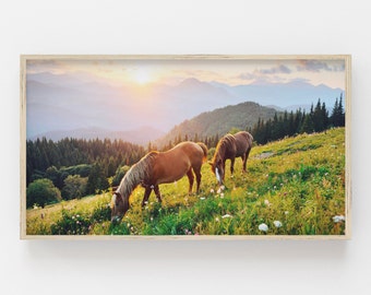 Puede incluir: Dos caballos marrones pastan en un exuberante prado verde con una cordillera de montañas al fondo. El sol se pone detrás de las montañas, proyectando un cálido resplandor sobre la escena.