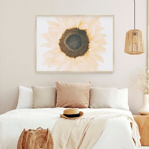 May include: A white bed with a white blanket and a brown wicker basket on the bed. There is a brown wicker lampshade hanging from the ceiling. A framed print of a close-up of a sunflower with a white background hangs on the wall behind the bed.