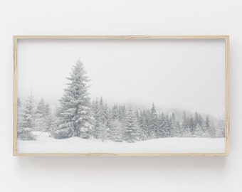 May include: A framed landscape print featuring a snowy forest scene. The image showcases snow-covered evergreen trees in a misty, winter environment. The artwork is encased in a light-colored wooden frame, creating a serene and natural aesthetic.