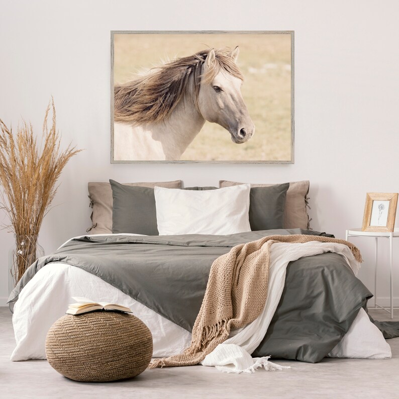 Peut inclure: Un cheval blanc avec une longue crini&egrave;re flottante se tient dans un champ. Le cheval regarde vers la droite de l'image. L'image est encadr&eacute;e et accroch&eacute;e &agrave; un mur blanc au-dessus d'un lit avec une couette grise et une couverture en fourrure beige.
