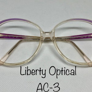 May include: Clear eyeglasses with a light purple accent on the top frame. The glasses have a rectangular shape with a rounded edge. The text "Liberty Optical" and "AC-3" are printed on the image.