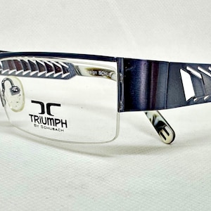 May include: Dark blue semi-rimless eyeglasses featuring a geometric cutout pattern on the temples. The lenses are printed with the text TRIUMPH BY SCHUBACH. The frame includes adjustable nose pads and patterned temple tips for a secure fit.