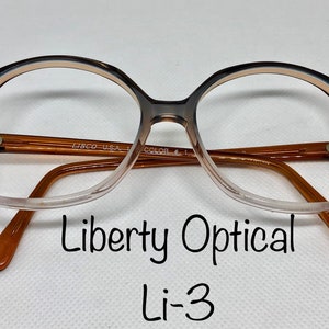 May include: Vintage Liberty Optical Li-3 eyeglasses. The frames are a gradient of brown and tan, with a rounded square shape. The arms and nose bridge are a solid brown color. The text "Liberty Optical" and "Li-3" are visible.