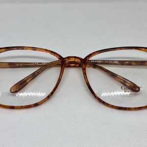 May include: A pair of eyeglasses with a tortoiseshell pattern on the frames. The lenses are clear, and the frames have a rectangular shape. The brand name "Gallery" is visible on the lower right lens.