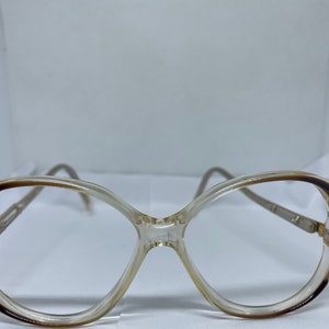 May include: A pair of clear plastic eyeglasses with brown accents. The glasses have a rounded, oval shape.