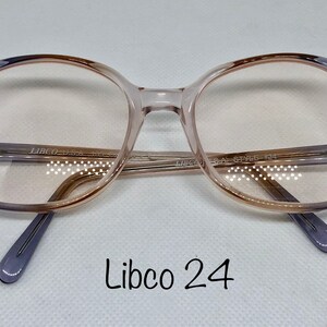 May include: Libco 24 eyeglasses with a gradient frame. The frames transition from a light purple to a brown hue, with a clear lens. The temples are a solid purple color. The text "Libco U.S.A." and "Style 134" are visible.