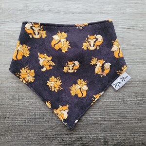 Puede incluir: Un pa&ntilde;uelo negro con un patr&oacute;n repetido de zorros naranjas y hojas amarillas. El pa&ntilde;uelo tiene una etiqueta blanca que dice "Mini Novas".