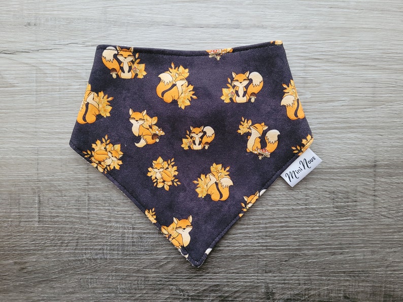Puede incluir: Un pa&ntilde;uelo negro con un patr&oacute;n repetido de zorros naranjas y hojas amarillas. El pa&ntilde;uelo tiene una etiqueta blanca que dice "Mini Novas".