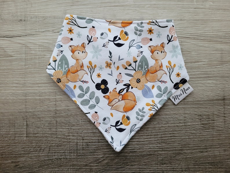 Puede incluir: Un bandana blanco con un patr&oacute;n de zorro y flores. El bandana tiene un esquema de color azul claro, amarillo, naranja y negro. El texto "Mini Nous" est&aacute; impreso en el bandana.