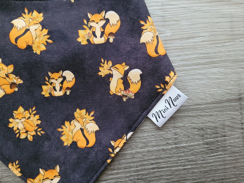 Puede incluir: Un bandana negro con un patr&oacute;n repetido de zorros naranjas y hojas de oto&ntilde;o. El bandana tiene una etiqueta blanca que dice "Mini Nous".