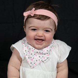 Puede incluir: Una ni&ntilde;a peque&ntilde;a con un vestido blanco y un babero de lunares rosa y gris. El babero tiene el texto "Mini  Moi". La ni&ntilde;a lleva una diadema rosa con un lazo.