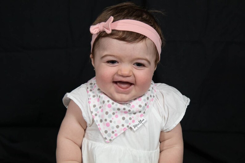 Puede incluir: Una ni&ntilde;a peque&ntilde;a con un vestido blanco y un babero de lunares rosa y gris. El babero tiene el texto "Mini  Moi". La ni&ntilde;a lleva una diadema rosa con un lazo.