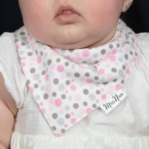 Puede incluir: Un babero blanco para beb&eacute; con un patr&oacute;n de lunares rosa y gris. El babero tiene una etiqueta blanca con el texto "Mini Nous" en &eacute;l.