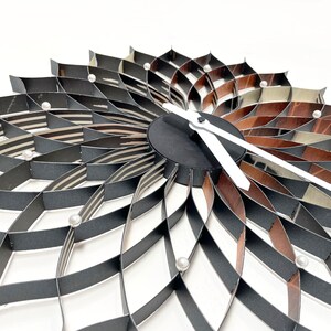 May include: A black and brown paper clock with white hands. The clock is shaped like a flower with multiple layers of paper.