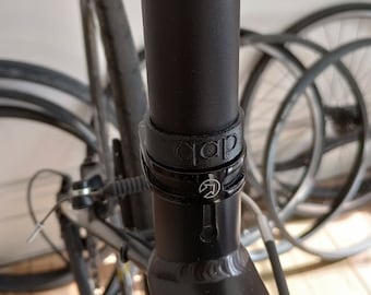 May include: Close-up of a black bicycle seat post with a black clamp and the word "qap" printed on it.
